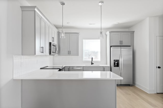 kitchen with gray cabinets, sink, hanging light fixtures, kitchen peninsula, and stainless steel appliances