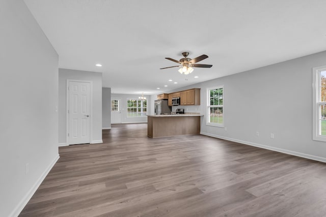 unfurnished living room with ceiling fan with notable chandelier and light hardwood / wood-style flooring