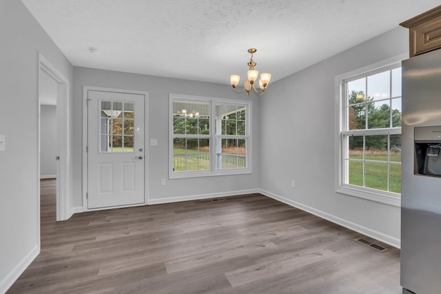 unfurnished dining area featuring a chandelier, a textured ceiling, and light hardwood / wood-style floors