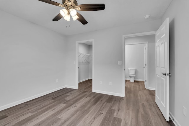 unfurnished bedroom featuring ceiling fan, a walk in closet, connected bathroom, a closet, and light wood-type flooring