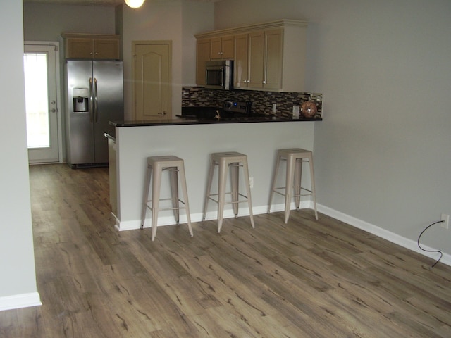 kitchen with appliances with stainless steel finishes, a breakfast bar, tasteful backsplash, kitchen peninsula, and hardwood / wood-style flooring