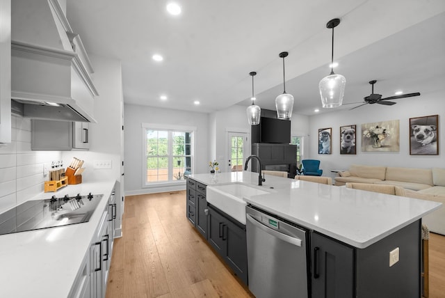 kitchen with light hardwood / wood-style floors, black electric stovetop, dishwasher, a center island with sink, and sink