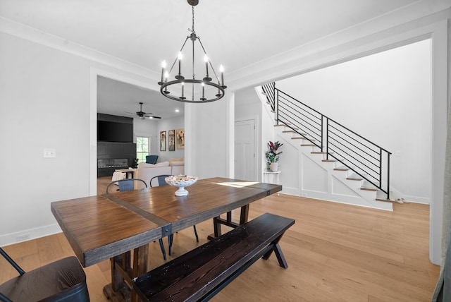 dining space with ceiling fan with notable chandelier, a tiled fireplace, light hardwood / wood-style floors, and crown molding