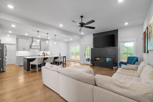 living room with ceiling fan, light hardwood / wood-style flooring, sink, and a healthy amount of sunlight