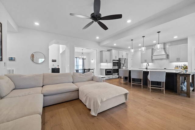 living room with ceiling fan with notable chandelier, sink, and light hardwood / wood-style flooring