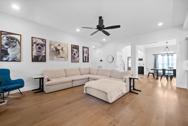 living room with ceiling fan with notable chandelier and light hardwood / wood-style flooring