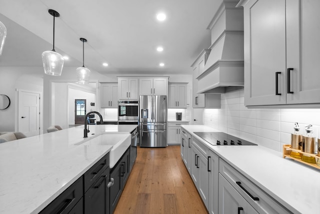 kitchen featuring stainless steel appliances, light hardwood / wood-style flooring, custom exhaust hood, decorative light fixtures, and sink