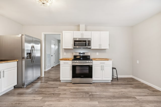 kitchen with appliances with stainless steel finishes, white cabinets, light wood-type flooring, and butcher block countertops