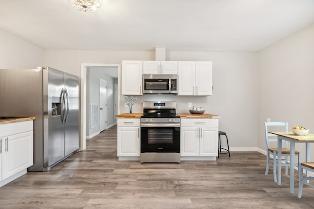 kitchen with white cabinets, wooden counters, stainless steel appliances, and light wood-type flooring