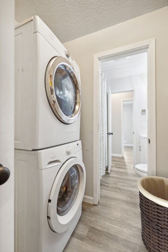 laundry area featuring stacked washer / drying machine, a textured ceiling, and light hardwood / wood-style floors