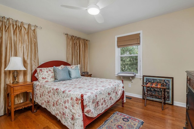 bedroom with a ceiling fan, visible vents, baseboards, and wood finished floors