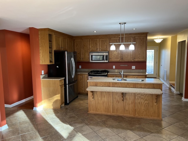 kitchen featuring stainless steel appliances, light countertops, hanging light fixtures, a sink, and an island with sink