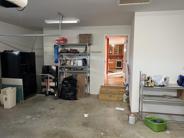 garage with black refrigerator with ice dispenser, wine cooler, and a garage door opener