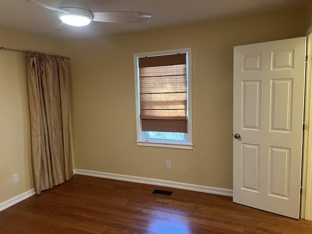 spare room featuring dark wood-type flooring, a ceiling fan, visible vents, and baseboards