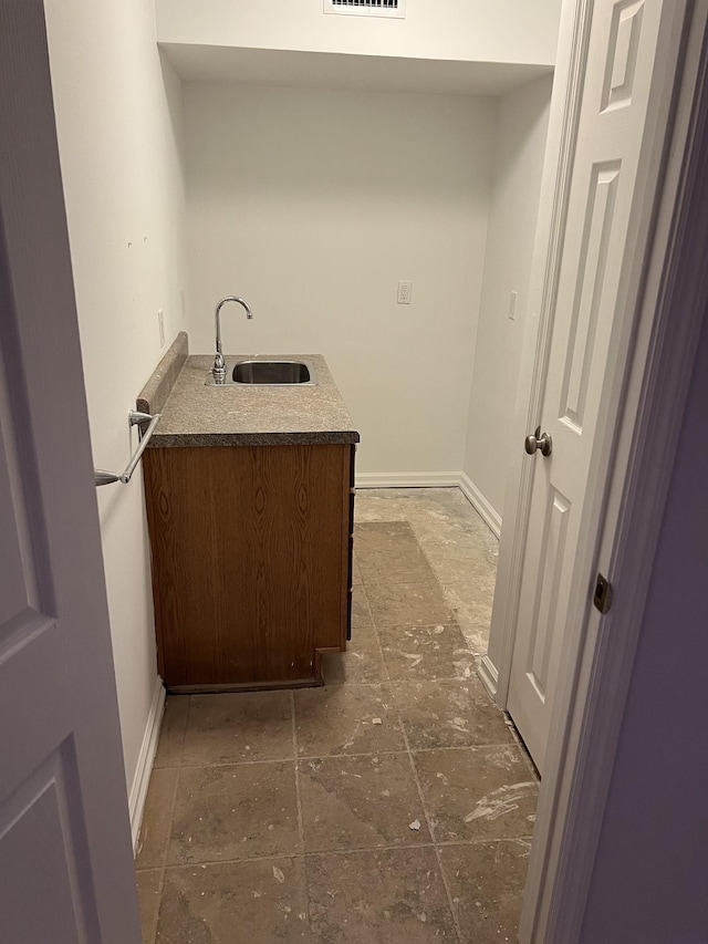 clothes washing area featuring stone tile flooring, a sink, visible vents, and baseboards