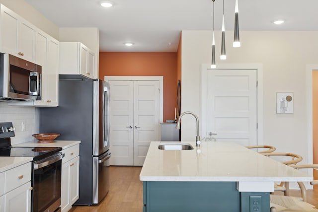 kitchen with light hardwood / wood-style floors, appliances with stainless steel finishes, hanging light fixtures, and a kitchen island with sink