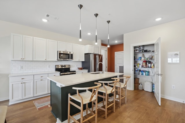 kitchen featuring white cabinets, hanging light fixtures, a kitchen island with sink, appliances with stainless steel finishes, and light hardwood / wood-style floors