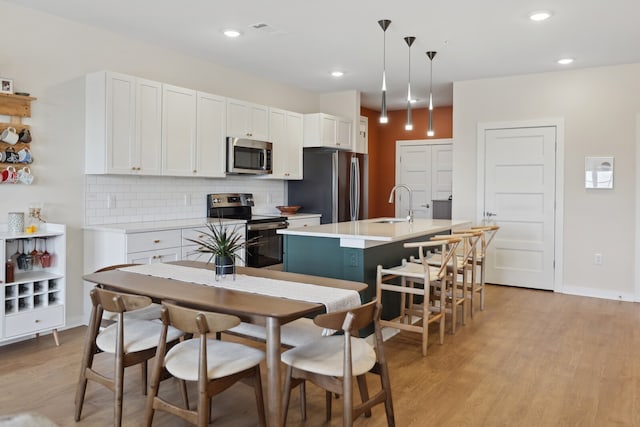 kitchen with white cabinets, an island with sink, decorative light fixtures, stainless steel appliances, and light wood-type flooring