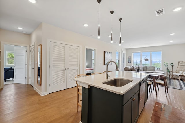 kitchen featuring dishwasher, light hardwood / wood-style flooring, decorative light fixtures, a center island with sink, and sink