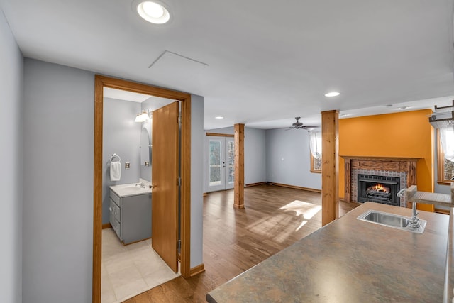 kitchen featuring ceiling fan, sink, gray cabinetry, a tile fireplace, and light wood-type flooring