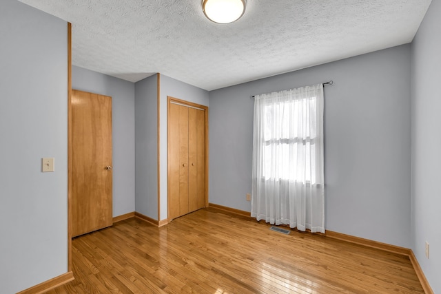 unfurnished bedroom with light wood-type flooring, a closet, and a textured ceiling