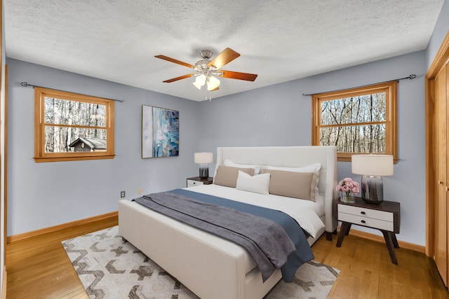 bedroom featuring ceiling fan, a textured ceiling, light hardwood / wood-style flooring, and multiple windows