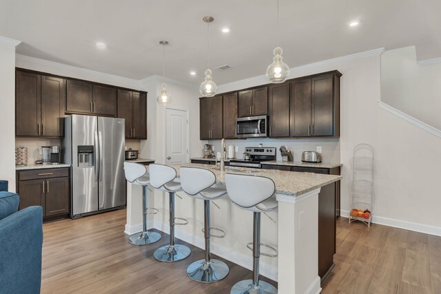 kitchen with pendant lighting, light hardwood / wood-style floors, a center island with sink, appliances with stainless steel finishes, and ornamental molding