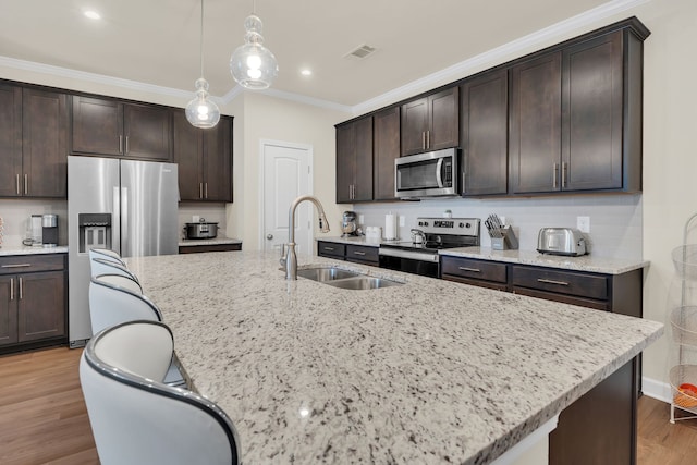 kitchen featuring appliances with stainless steel finishes, wood-type flooring, dark brown cabinets, and an island with sink