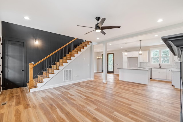 unfurnished living room featuring a sink, visible vents, light wood finished floors, a ceiling fan, and stairs