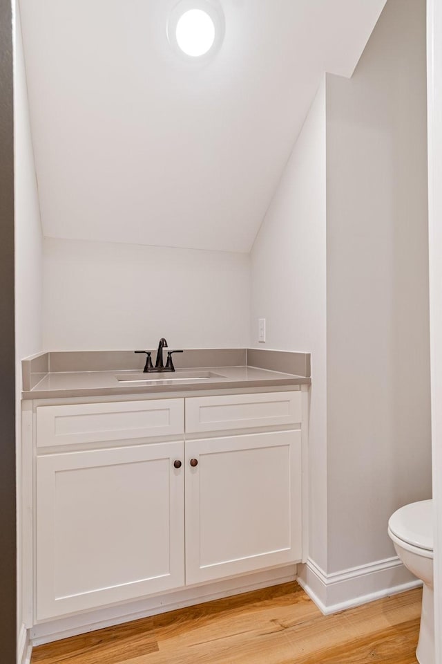 bathroom with vanity, lofted ceiling, toilet, baseboards, and wood finished floors