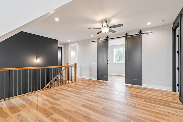 spare room featuring recessed lighting, a barn door, baseboards, light wood-type flooring, and a ceiling fan