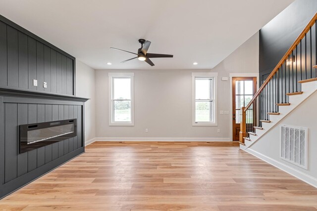 unfurnished living room featuring light wood-type flooring, plenty of natural light, visible vents, and a glass covered fireplace