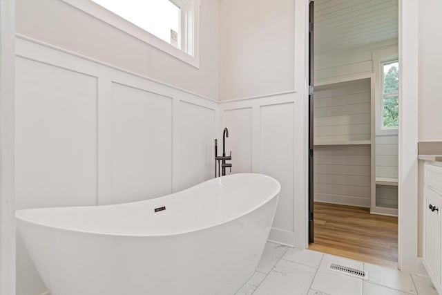 bathroom featuring visible vents, a freestanding tub, a decorative wall, marble finish floor, and wainscoting