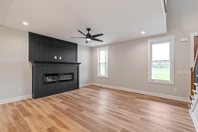 unfurnished living room featuring light wood finished floors, a large fireplace, baseboards, and a healthy amount of sunlight