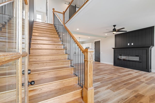 stairs with baseboards, recessed lighting, a fireplace, wood finished floors, and a ceiling fan