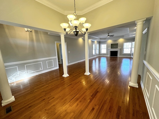 unfurnished living room with crown molding, dark wood-type flooring, ceiling fan with notable chandelier, and decorative columns