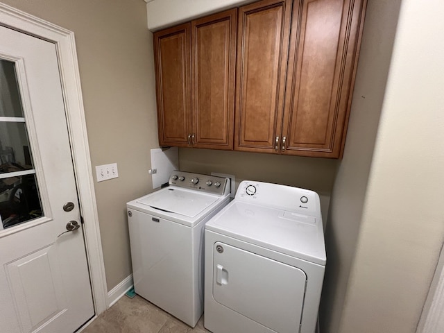 clothes washing area featuring separate washer and dryer, light tile patterned floors, and cabinets