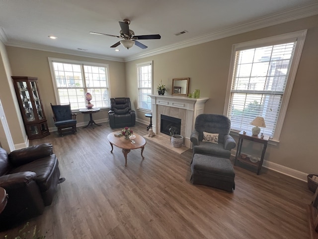 living room featuring ornamental molding, a tiled fireplace, ceiling fan, and dark wood-type flooring