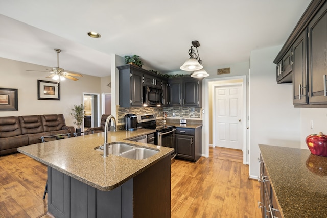 kitchen featuring hanging light fixtures, sink, stainless steel stove, a kitchen breakfast bar, and light hardwood / wood-style floors