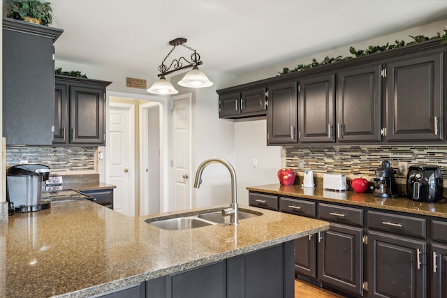 kitchen with pendant lighting, sink, light hardwood / wood-style flooring, backsplash, and dark stone countertops