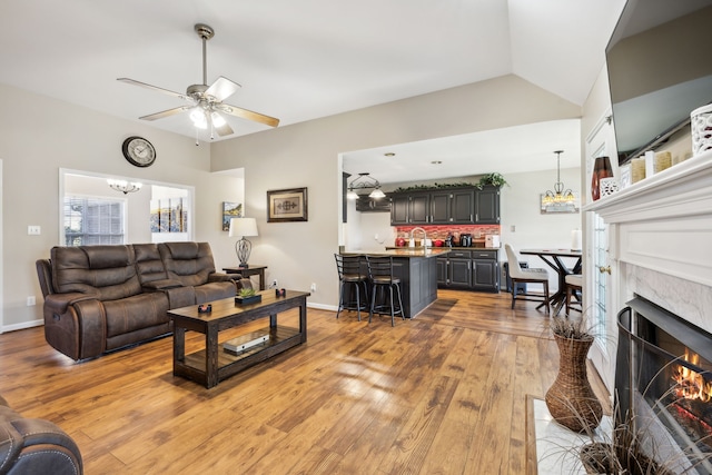 living room with ceiling fan with notable chandelier, sink, light hardwood / wood-style flooring, and vaulted ceiling