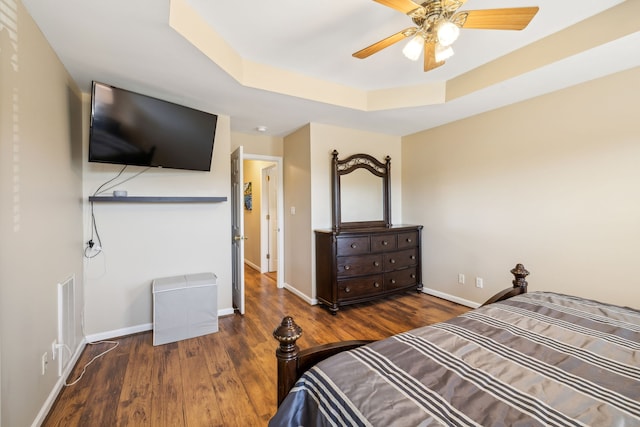 bedroom with a raised ceiling, dark hardwood / wood-style floors, and ceiling fan