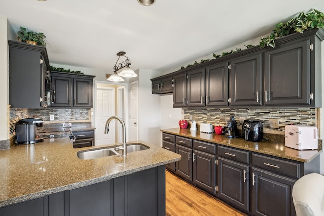 kitchen with light wood-type flooring, tasteful backsplash, sink, pendant lighting, and dark stone counters