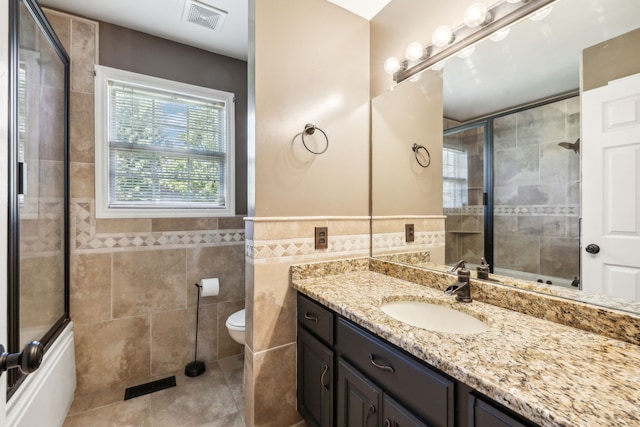 full bathroom featuring vanity, combined bath / shower with glass door, tile patterned floors, tile walls, and toilet