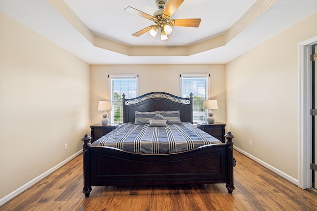 bedroom with a raised ceiling, wood-type flooring, and ceiling fan