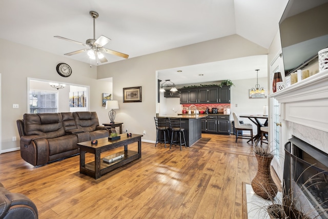 living room featuring lofted ceiling, ceiling fan with notable chandelier, light hardwood / wood-style floors, and sink