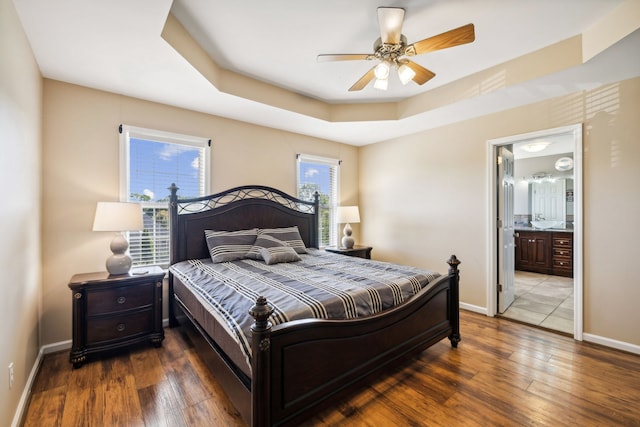 bedroom with wood-type flooring, a raised ceiling, connected bathroom, and ceiling fan