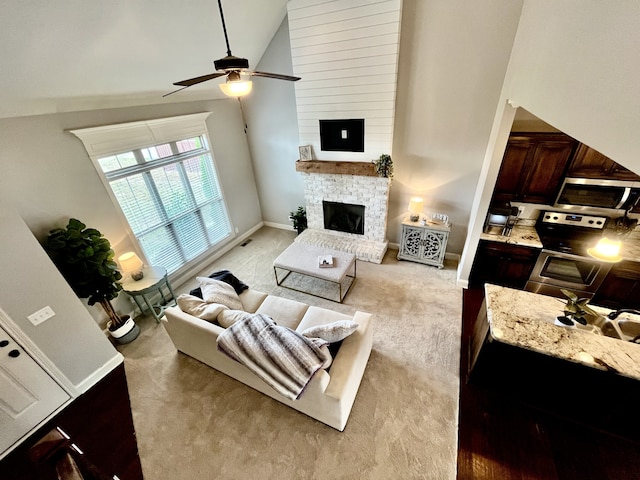 living room featuring light carpet, a stone fireplace, ceiling fan, and lofted ceiling