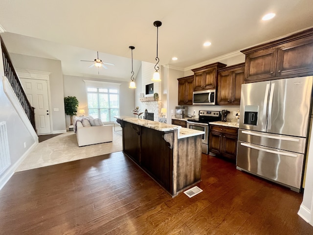 kitchen with a kitchen breakfast bar, stainless steel appliances, dark wood-type flooring, a kitchen island, and hanging light fixtures