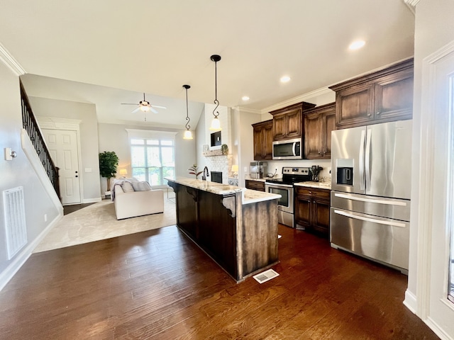 kitchen featuring pendant lighting, a center island with sink, appliances with stainless steel finishes, a kitchen bar, and dark brown cabinetry